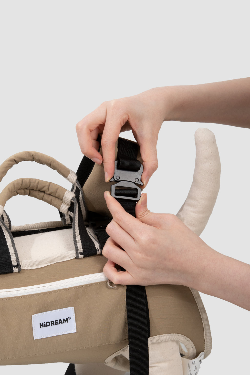 Person adjusting a strap on a pet carrier with 'HIDREAM' label against a white background