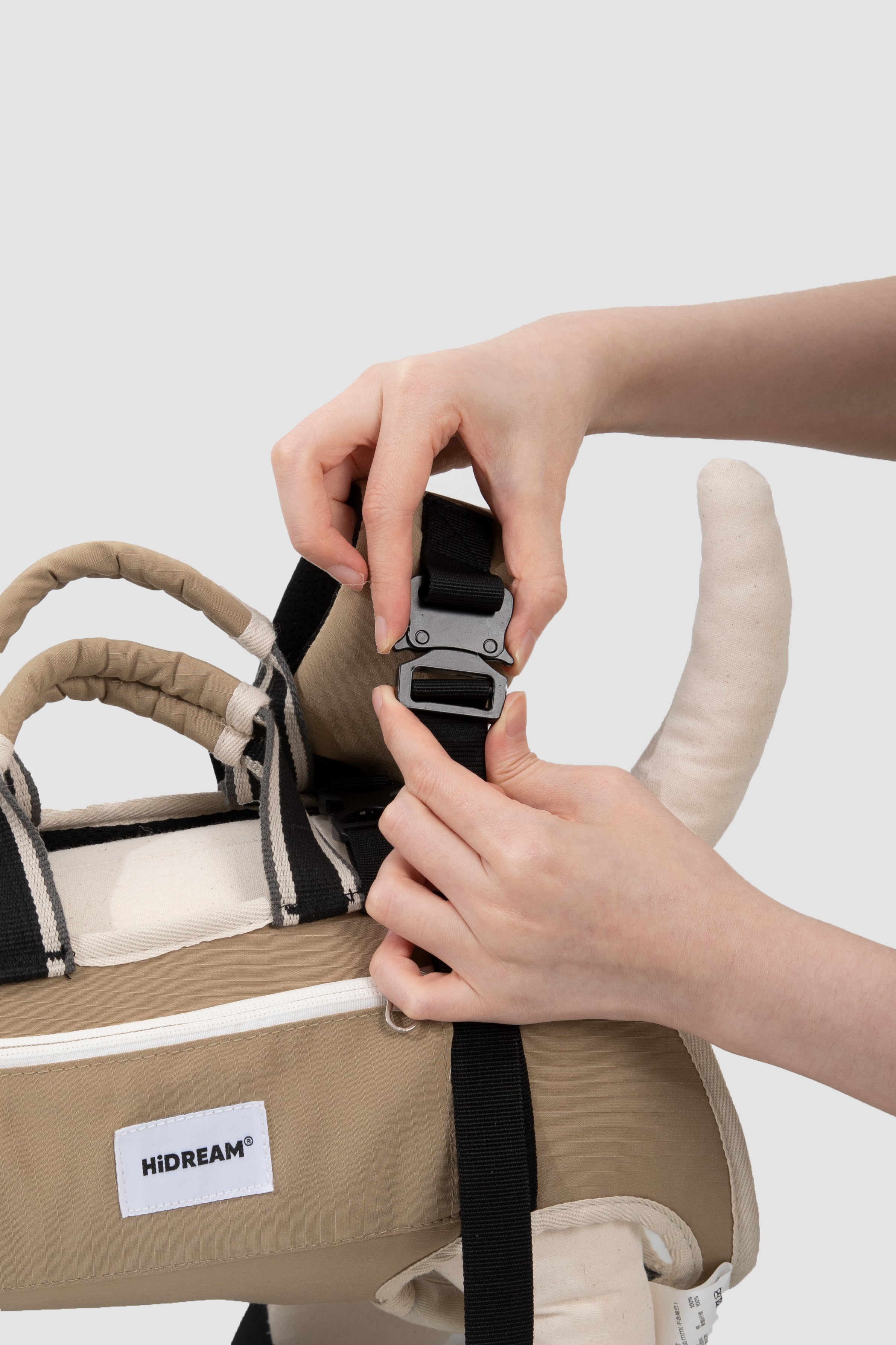 Person adjusting a strap on a pet carrier with 'HIDREAM' label against a white background